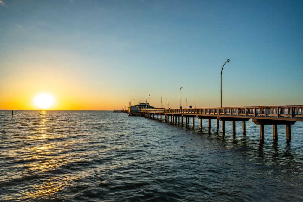 Tranquil scene of a sunset over Fairhope Pier in Alabama with a clear sky and calm sea.